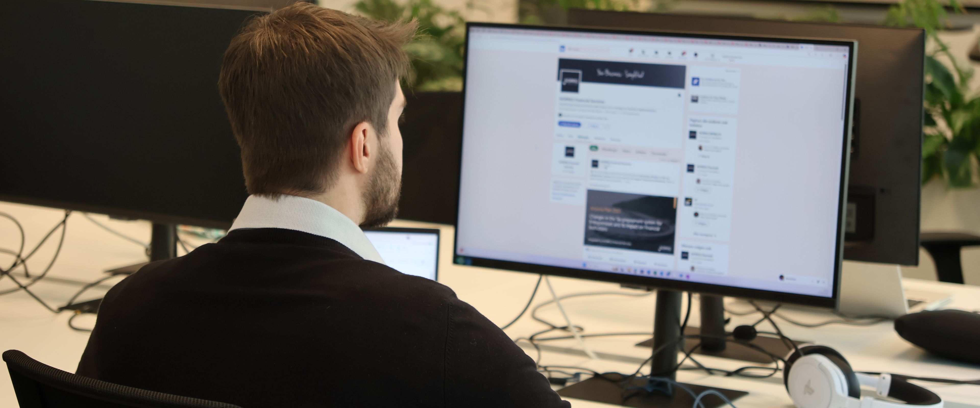 Person working on a computer in an office with headphones nearby.