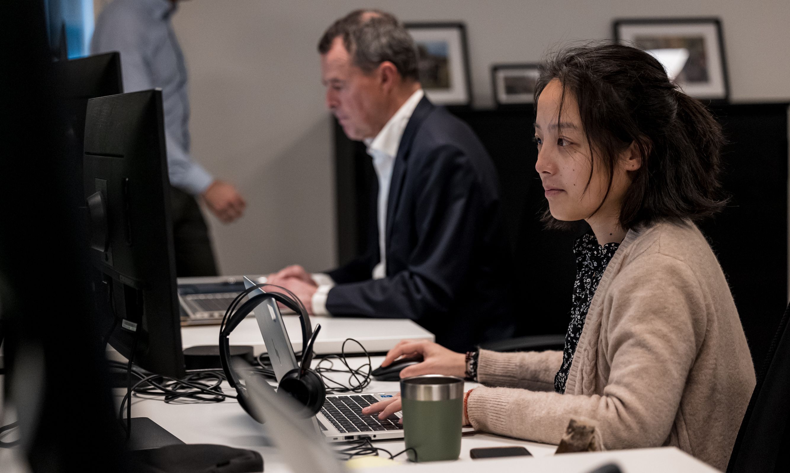 People working at computers with headphones and a coffee cup.