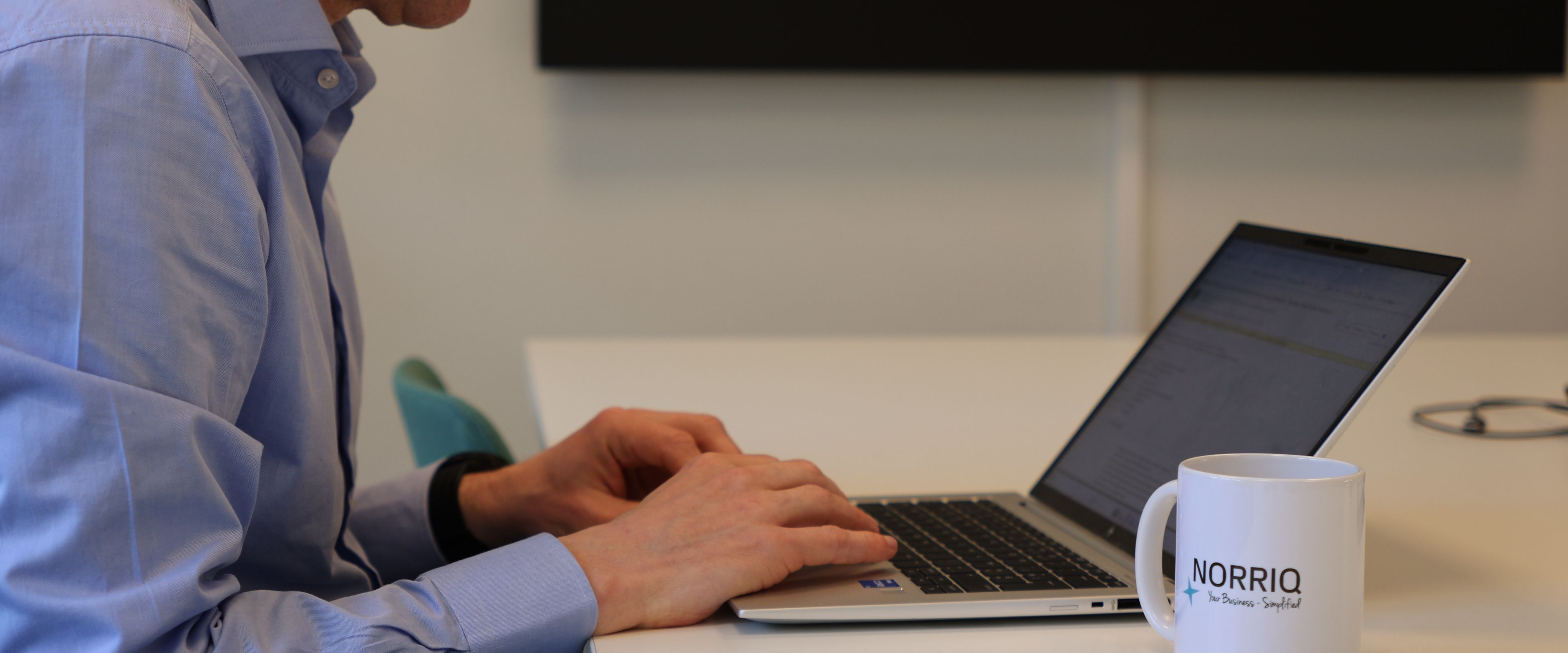 A person typing on a laptop at a desk with a NORRIQ mug