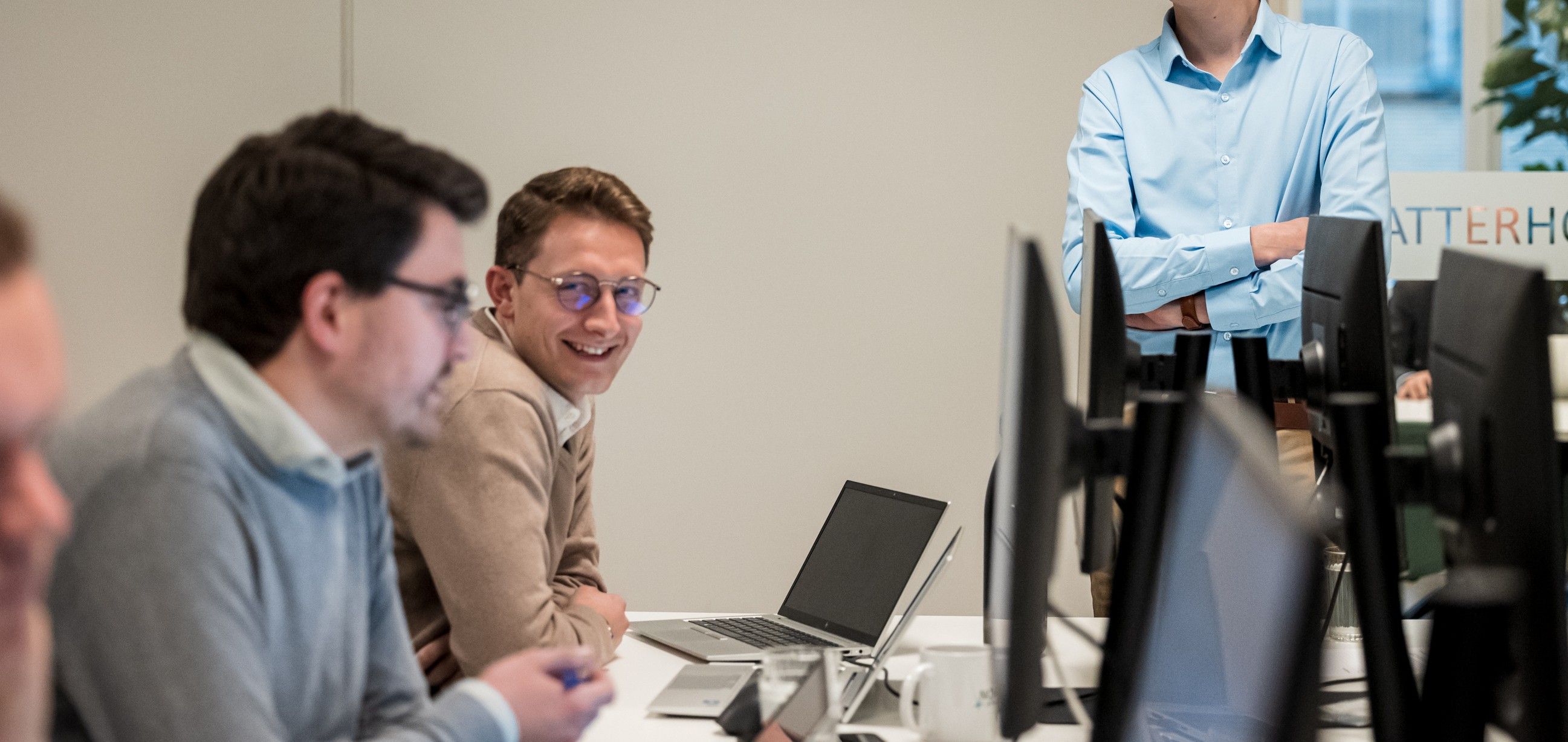 Group of colleagues working at computers, engaged in a discussion in a modern office setting.