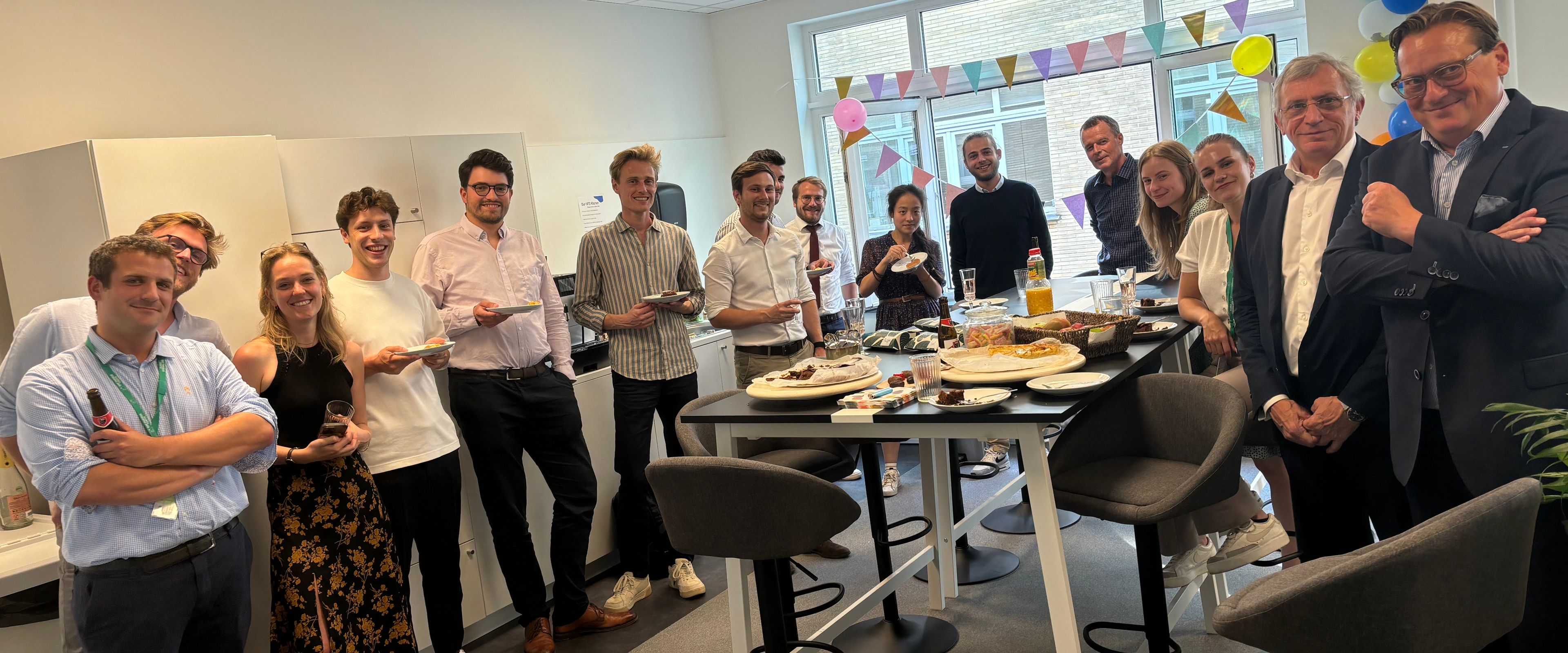 Group of people gathered in an office kitchen area for a celebration