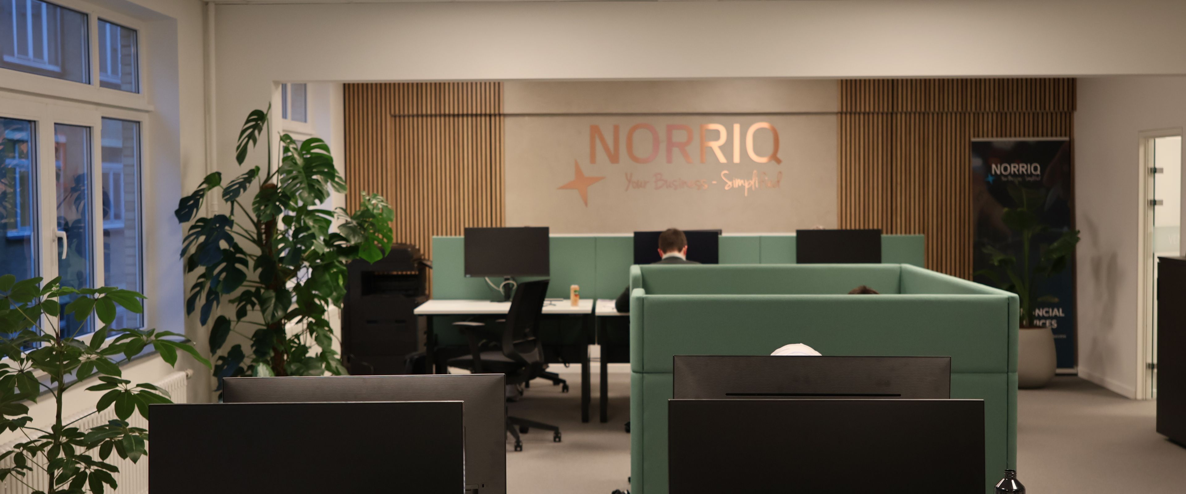 Open office space with desks, computers, and the NORRIQ logo on the wall