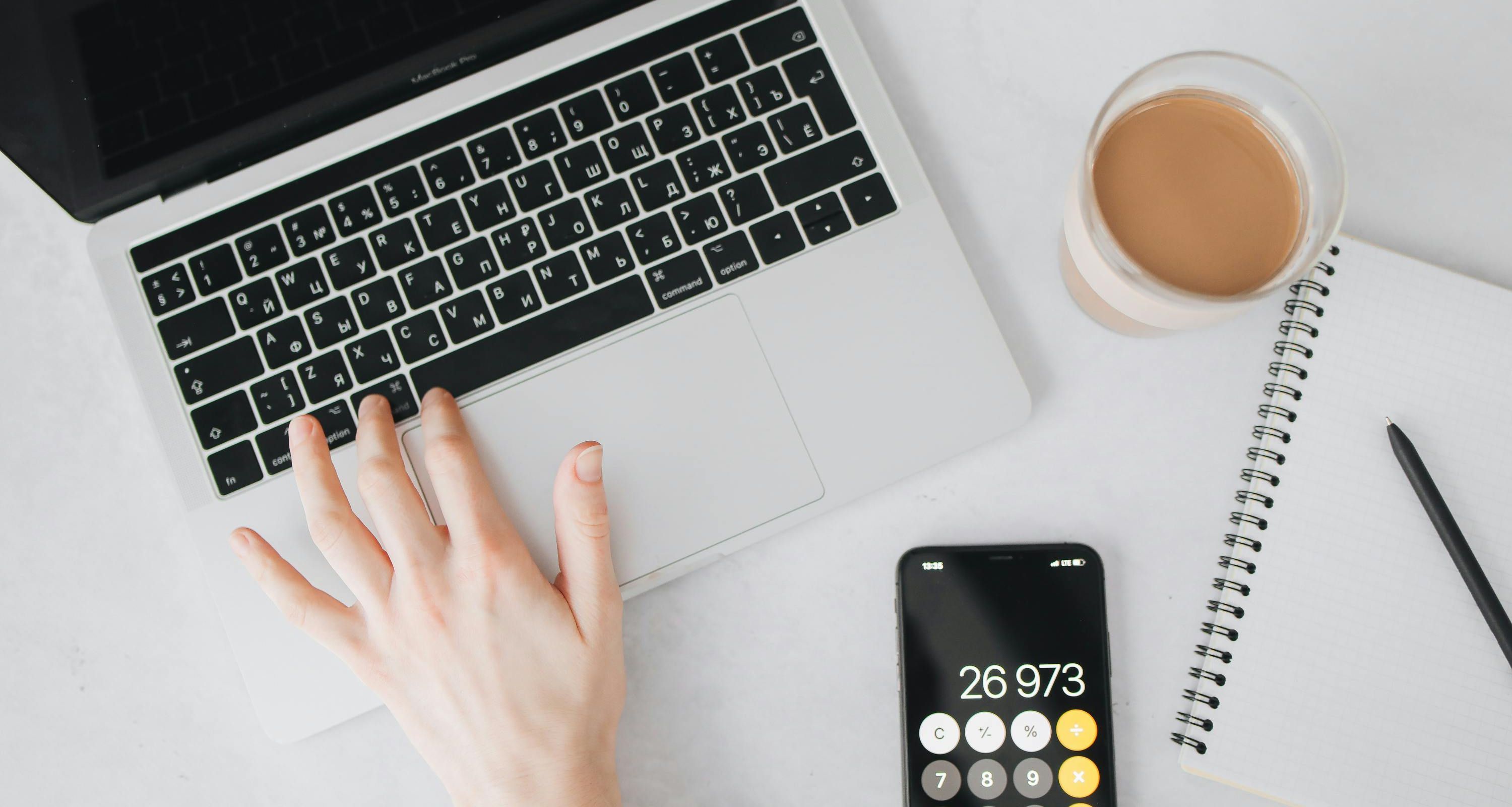 Hand op laptop met tas koffie en rekentoestel